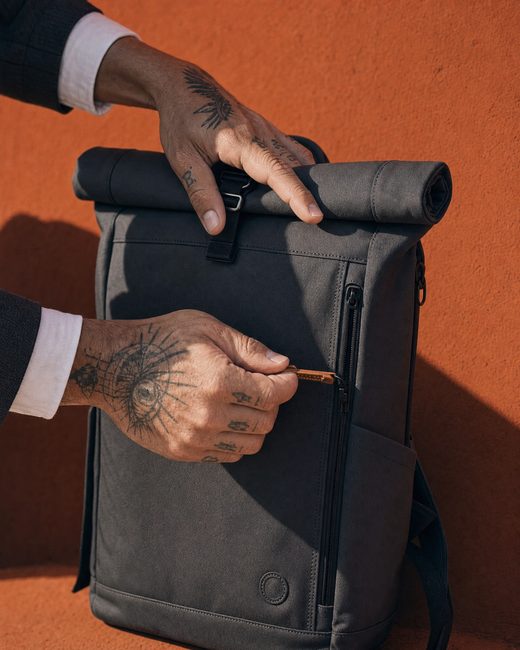 Hands adjusting the backpack against a rust wall